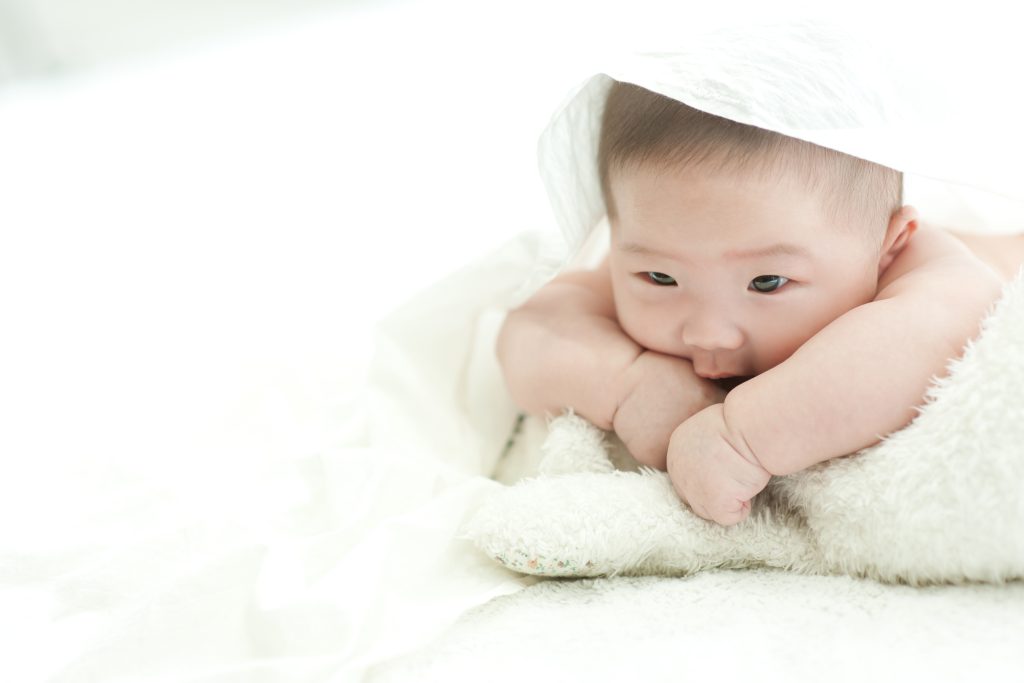 baby is staring front white bed with white background