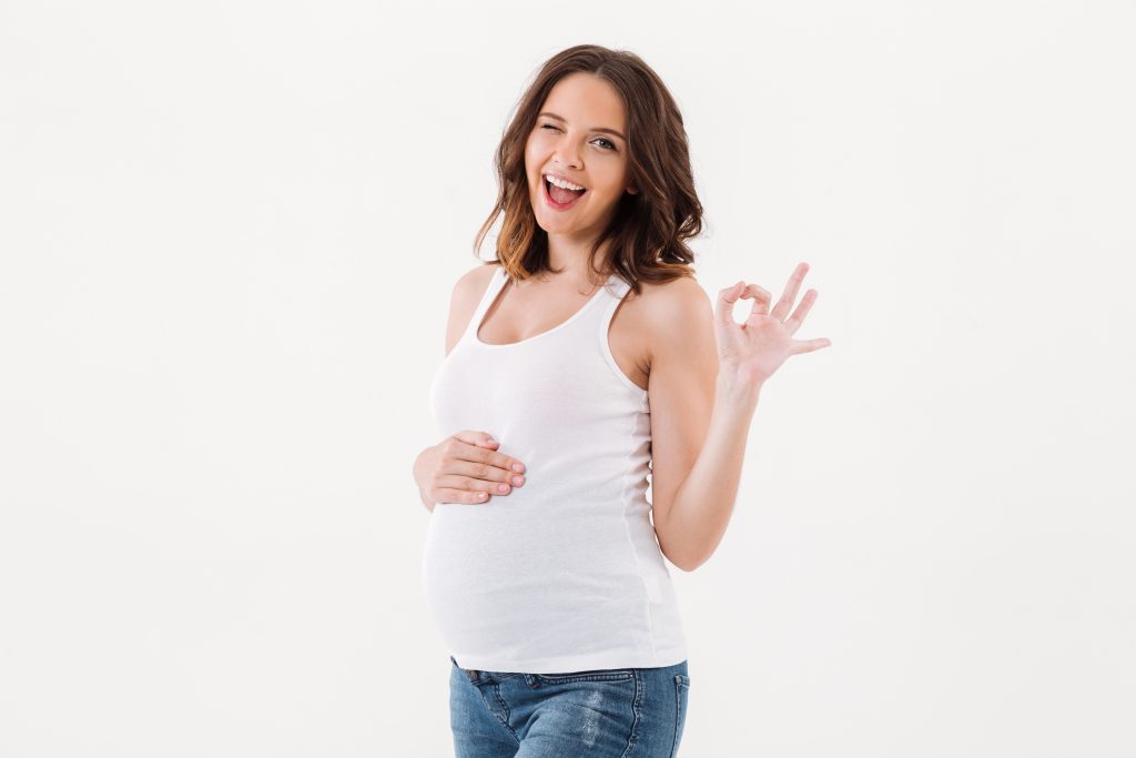 cheerful pregnant woman showing okay gesture