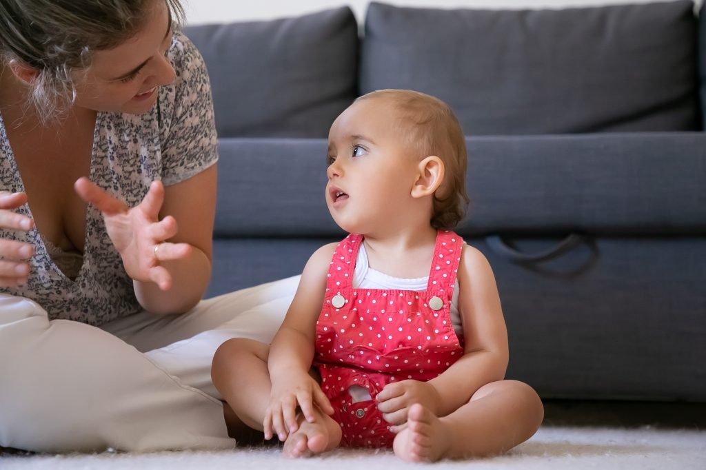 cute little girl listening mom with open mouth looking her cropped mother sitting cross legged floor talking daughter lovely infant sitting barefoot weekend motherhood concept
